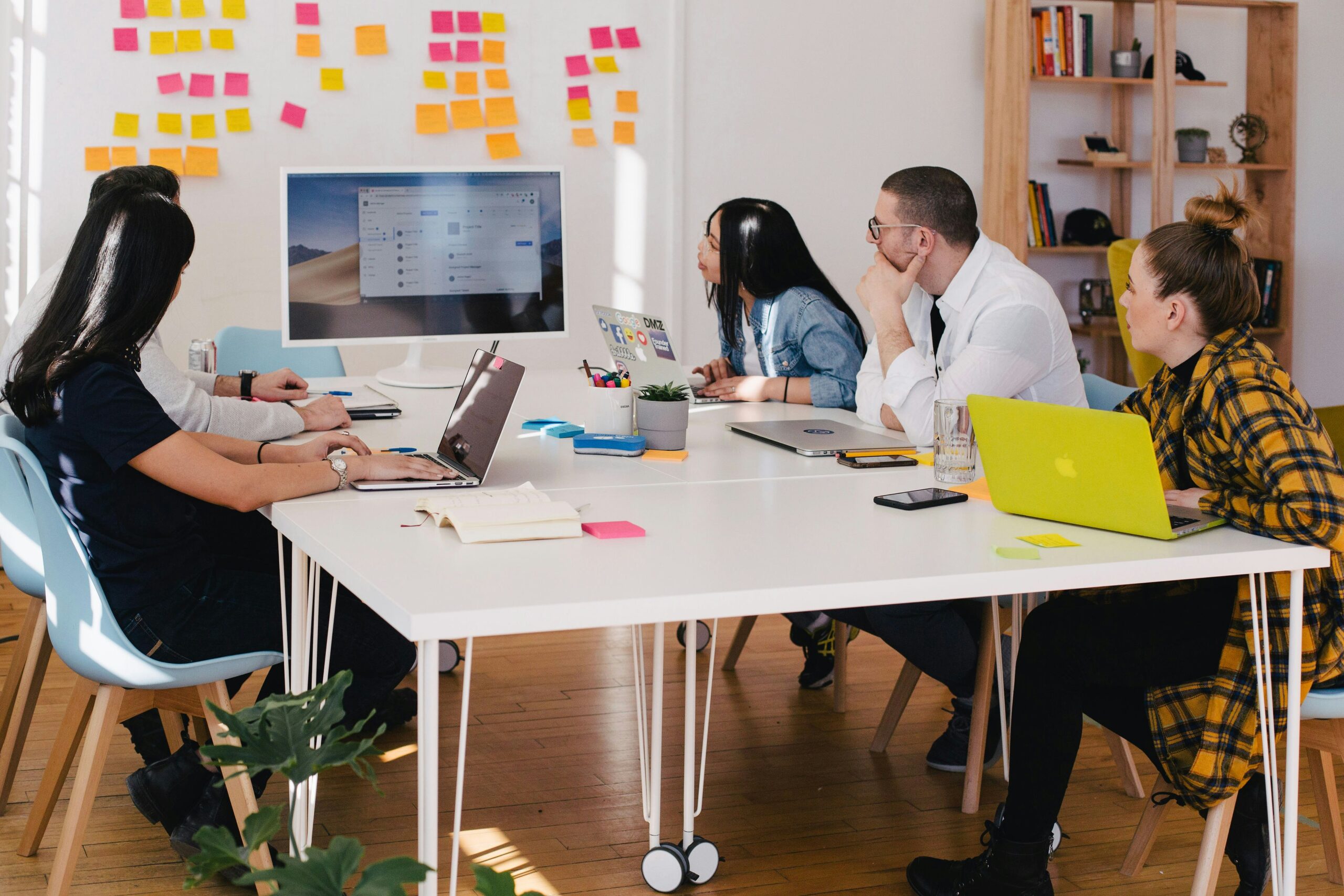 Titelbild zur Leistung "Start-up-Creation", das einen Schreibtisch in einem Büro zeigt, an dem fünf Mitarbeitende mit ihren Laptops sitzen und auf einen Bildschirm am Tischende blicken.